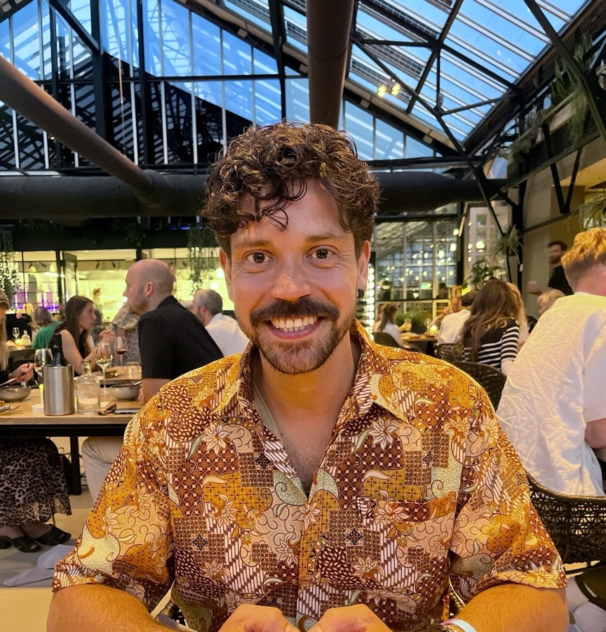 Dei Martinez Elurbe smiling at a restaurant table under the glass roof of a greenhouse dining room